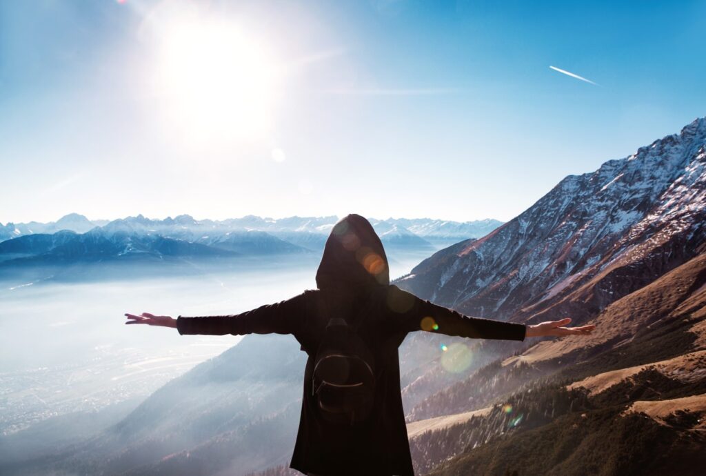 A woman with her hands in the air atop a beautiful mountain peak 