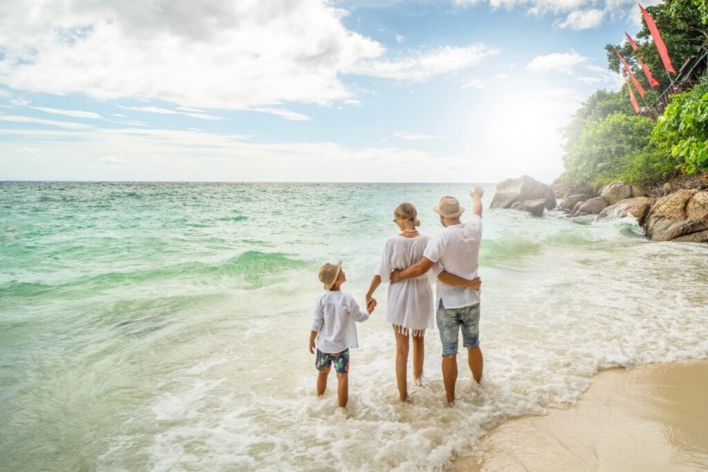 Mom, dad, and son at a white beach looking upon blue waters in a scenic, dreamy complexion. 