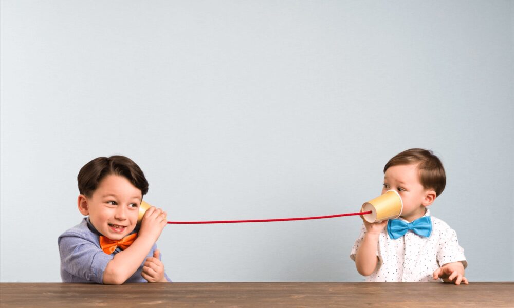 Two children using paper cups and a string to play the telephone game