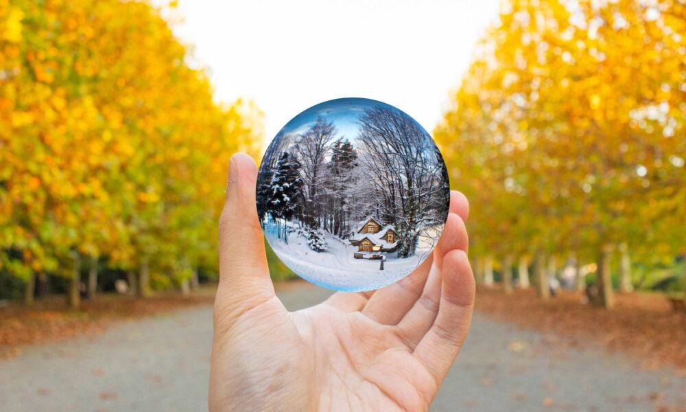 January Brain Concept. A hand holding a crystal ball surrounded by autumn trees. The crystal ball contains a winter landscape.