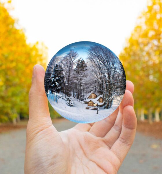 January Brain Concept. A hand holding a crystal ball surrounded by autumn trees. The crystal ball contains a winter landscape.