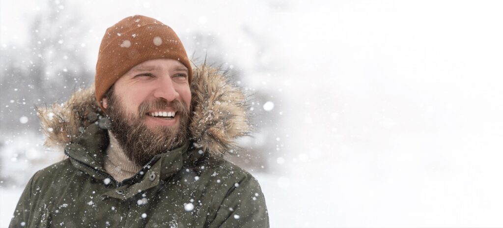 a man in a hat and jacket in the snow, smiling 
